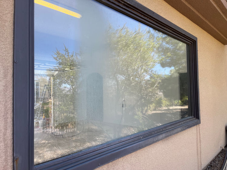 Large picture window on a Las Vegas stucco home with severe hard water etching and milky mineral film before professional treatment