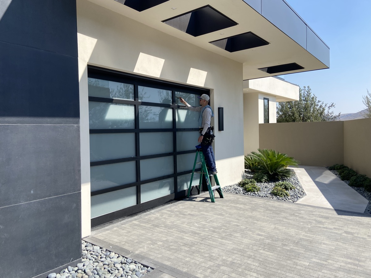 Neon Window Cleaning technician on a ladder cleaning frosted glass panels on a modern Summerlin luxury home