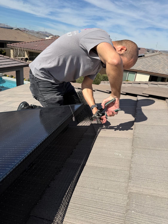 Neon Window Cleaning technician fastening pigeon guard mesh clips to solar panel frames on a Las Vegas residential rooftop